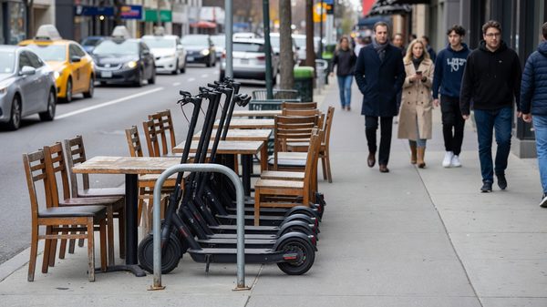 Sidewalk furniture zone with shared e-scooters and e-bikes parked upright beside a bike rack