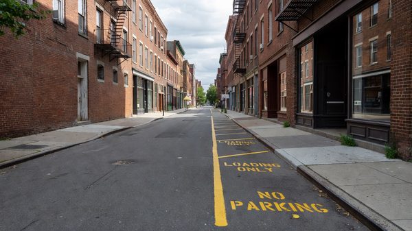Narrow city street lined with brick storefronts and a marked curbside loading area
