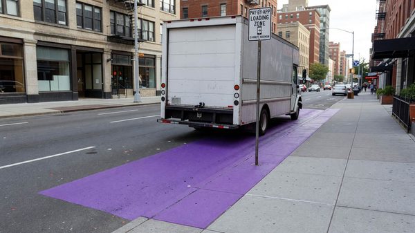 Purple-painted curbside loading zone on a city street with a delivery truck parked beside pay-by-app signage