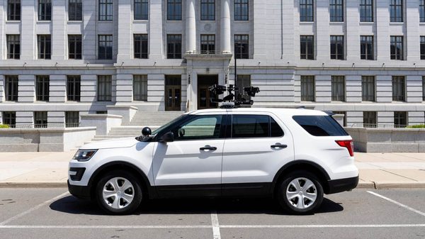 Parking enforcement vehicle with a roof-mounted license plate camera parked on a street near a state government building