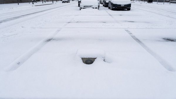 Snow-covered on-street parking spaces with an in-ground sensor housing partially obscured by drifted snow